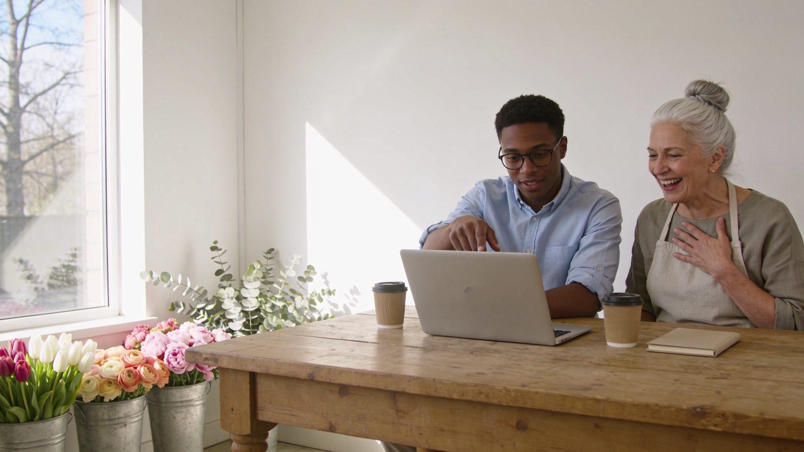 Illustrative image — an accountant going over the books on a laptop with a flower shop owner, who is laughing